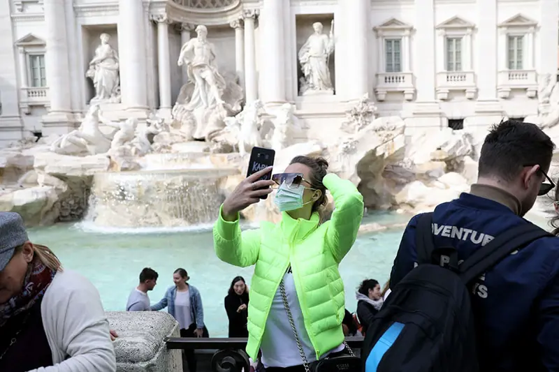 En kvinna med ansiktsmask tar en selfie framför Fontana di Trevi i Rom